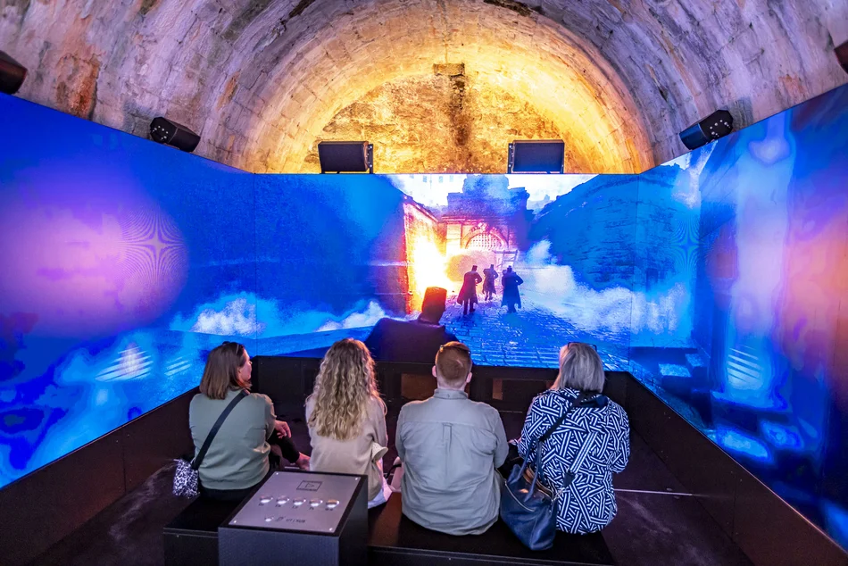 Immersives Erlebnis: Sturm auf den Königstein Vier Besucherinnen sitzen vor einer LED-Wall und schauen sich das Szenario eines Angriffs auf die Festung Königstein an.