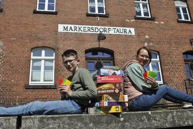 Ein Junge und ein Mädchen sitzen auf der Bahnsteigkante des Museumsbahnhofs Markersdorf-Taura, zwischen ihnen ein Stapel Brettspiele.