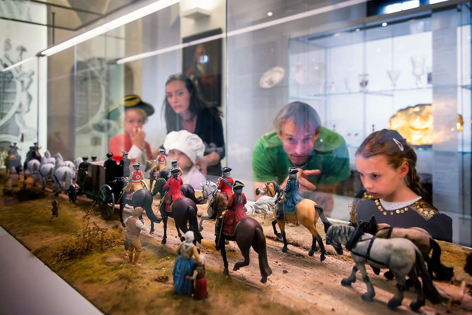 Eine Familie betrachtet das Modell eines Kutschenzuges in einer Glasvitrine.