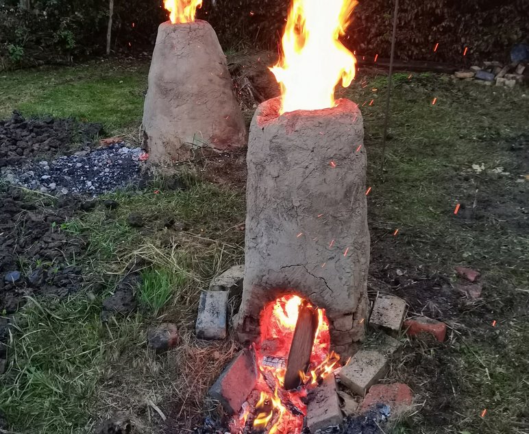 Das Foto zeigt einen selbst gebauten Rennofen (eine Vorrichtung aus Lehm zur Gewinnung von Eisen aus Eisenerz), darin lodert ein Feuer.