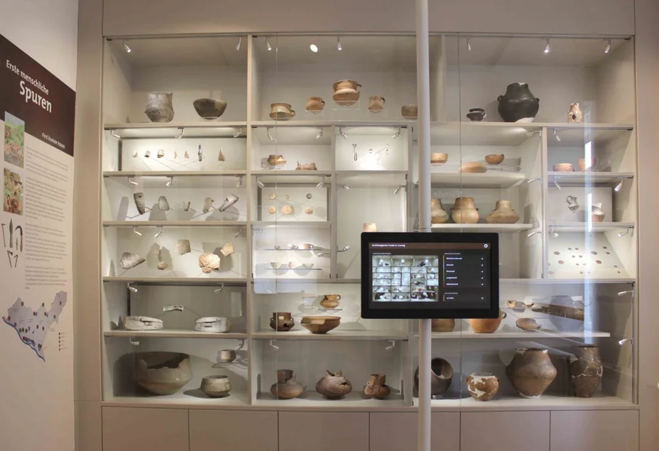 Archäologische Funde in Coswig Eine wandfüllende Vitrine beherbergt eine Vielzahl archäologischer Fundstücke. Vor der Vitrine ist ein digitales Touchpad angebracht.