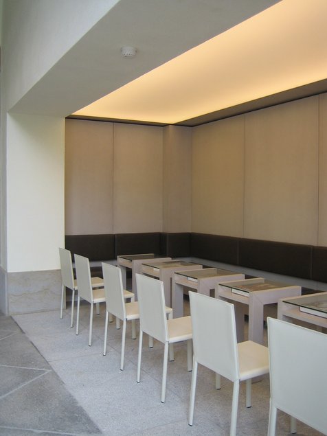 Das Foto zeigt einen Blick in das Café im Foyer der Kunstsammlungen am Theaterplatz mit sechs weißen Stühlen und Tischen sowie einer an der Wand verlaufenden langen Sitzbank.
