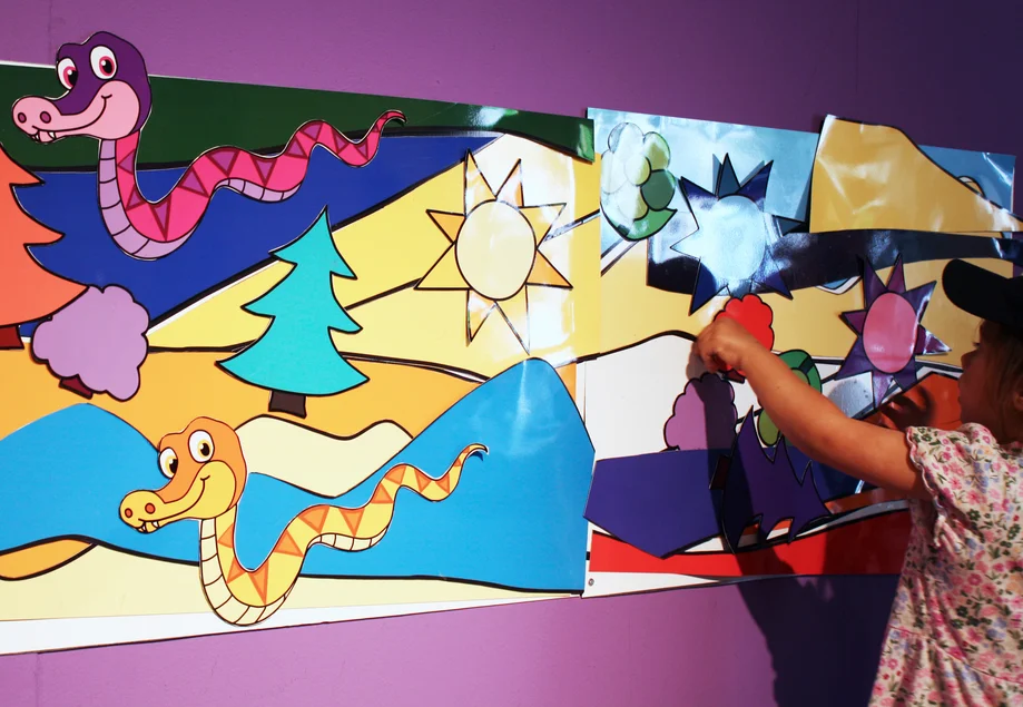 Farbpuzzle in der Sonderausstellung „More than Colours“ Ein Kind beschäftigt sich an einem großen, bunten, diverse Tier- und Pflanzenfiguren enthaltenden Wand-Puzzle.