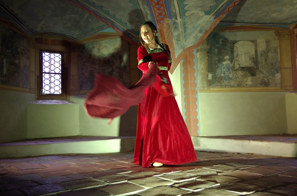 Eine Frau in rotem Kleid schwingt tanzend ein rotes Tuch in einem historischen Saal von Burg Mildenstein.