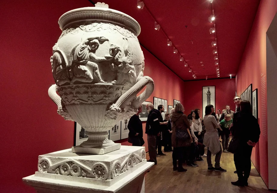 Im Vordergrund steht eine antike Porzellanvase, im Hintergrund verschwommen Menschen in der Ausstellung eines Museums.