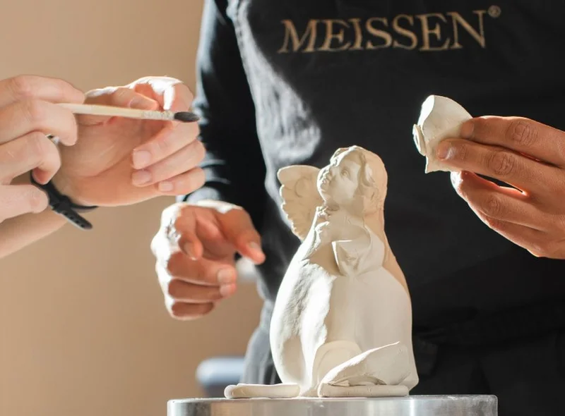 Im Kreativ-Workshop bei MEISSEN gestalten Hände mit feinen Werkzeugen eine Porzellan-Engelsfigur – konzentrierte Atmosphäre.