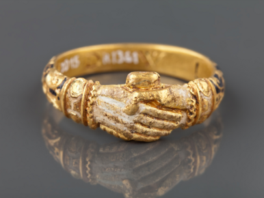 Das Bild zeigt einen goldenen Ring in Form von verschränkten Händen.