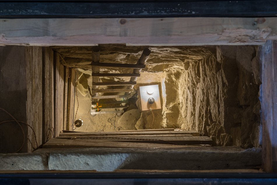 Foto eines in ein historisches Gemäuer gegrabenen Tunnels mit selbstgebauten Lampen und Leitern