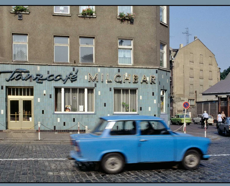 Ein kleiner, blauer Pkw der DDR-Marke Trabant fährt am Wurzener "Tanzcafé Milchbar" vorbei.