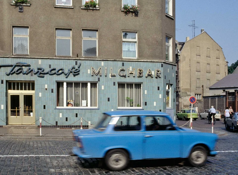 Ein kleiner, blauer Pkw der DDR-Marke Trabant fährt am Wurzener "Tanzcafé Milchbar" vorbei.