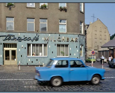 Ein kleiner, blauer Pkw der DDR-Marke Trabant fährt am Wurzener "Tanzcafé Milchbar" vorbei.