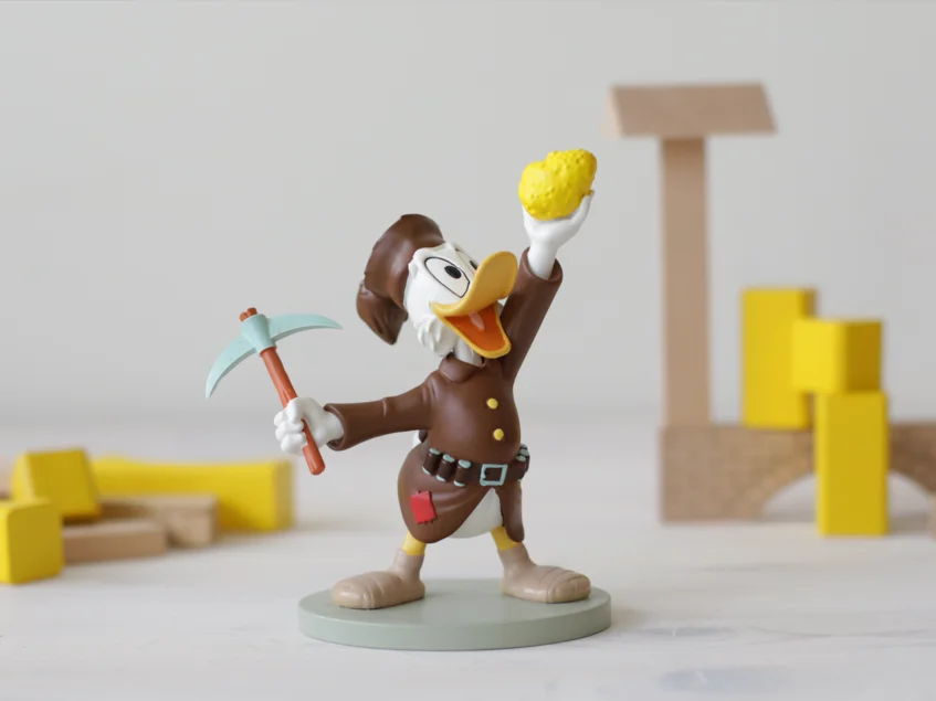 Barbara und die Hunte Das Bild zeigt die Comic-Figur Dagobert Duck. Sie hält ein Stück Gold in der einen und eine Hacke in der anderen Hand.