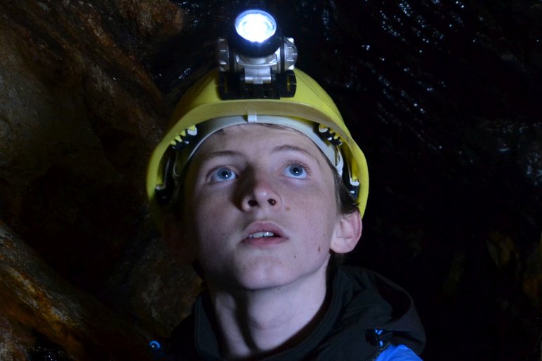 Foto eines Jungen mit Grubenhelm und Stirnlampe in einem Bergwerksstollen