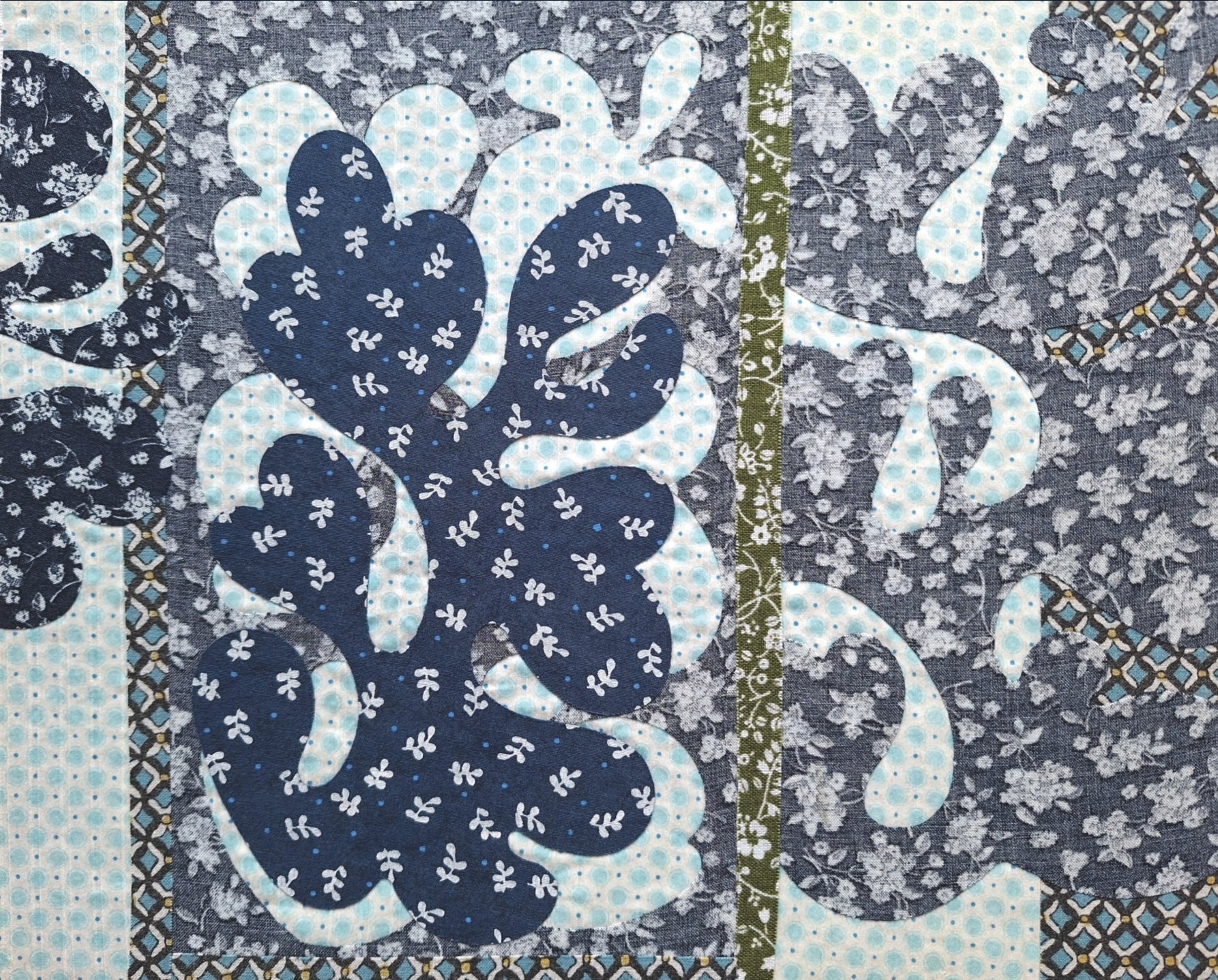 In Blau-, Grau- und Grüntönen auf hellen Grund applizierte florale Motive aus Textil