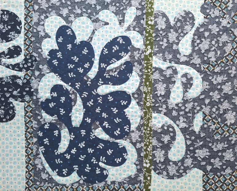 In Blau-, Grau- und Grüntönen auf hellen Grund applizierte florale Motive aus Textil