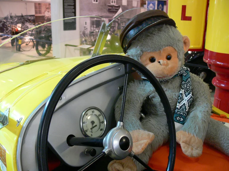 Ein Plüschaffe sitzt neben dem Lenkrad eines historischen Spielautos.