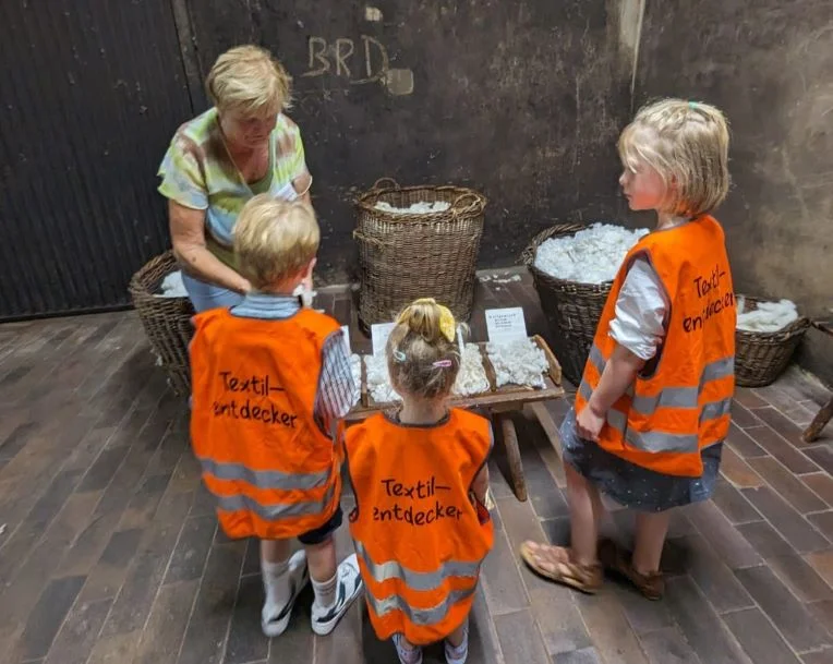 Wie fühlt sich Wolle an? Drei junge Schüler nehmen unter Anleitung einer Frau Woll-Proben in die Hand.