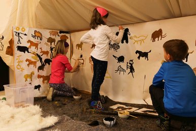 Kinder malen eiszeitliche Motive an Wände, die wie eine Eiszeithöhle anmuten