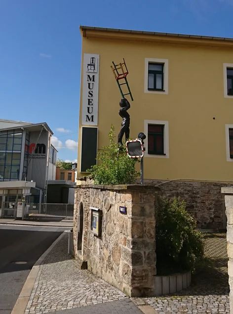 Vor dem Museumsgebäude steht die moderne Skulptur einer Person, die einen Stuhl in die Höhe hält.