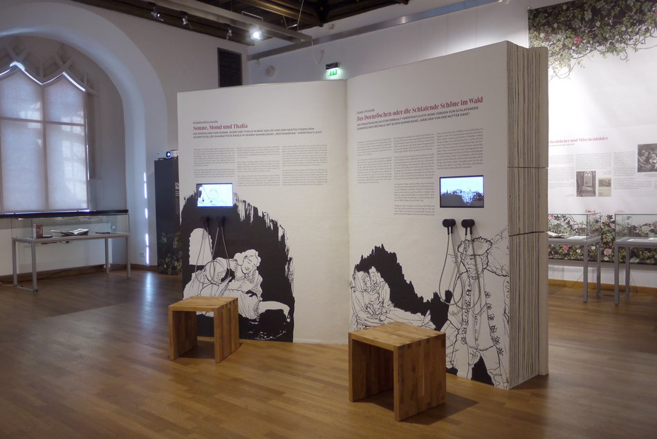 Eine Medienstation in Form eines etwa zwei Meter hohen aufgeschlagenen Buches steht in einem Ausstellungsraum. Dieses „interaktive Buch“ enthält Texte, Videos und Hörstationen.
