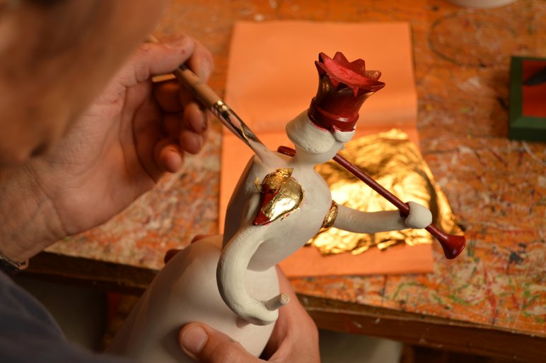 Nahaufname der Hand eines Künstlers, der auf den Schultern einer Engelsfigur mit einem Pinsel Blattgold auflegt