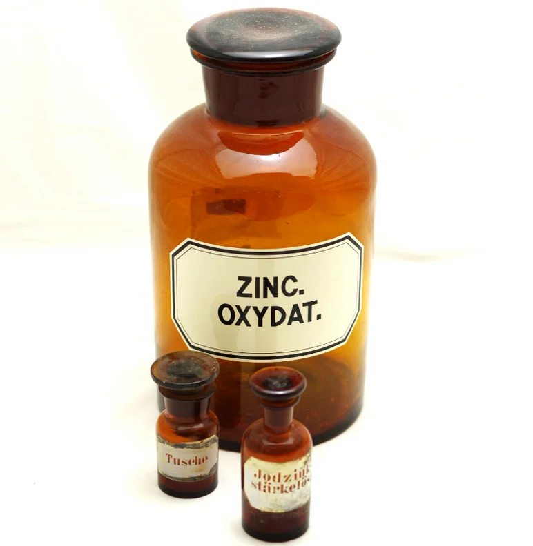 Drei historische Apotheker-Fläschchen aus braunem Glas, die größte ist etikettiert mit den Worten "Zinc Oxydat".