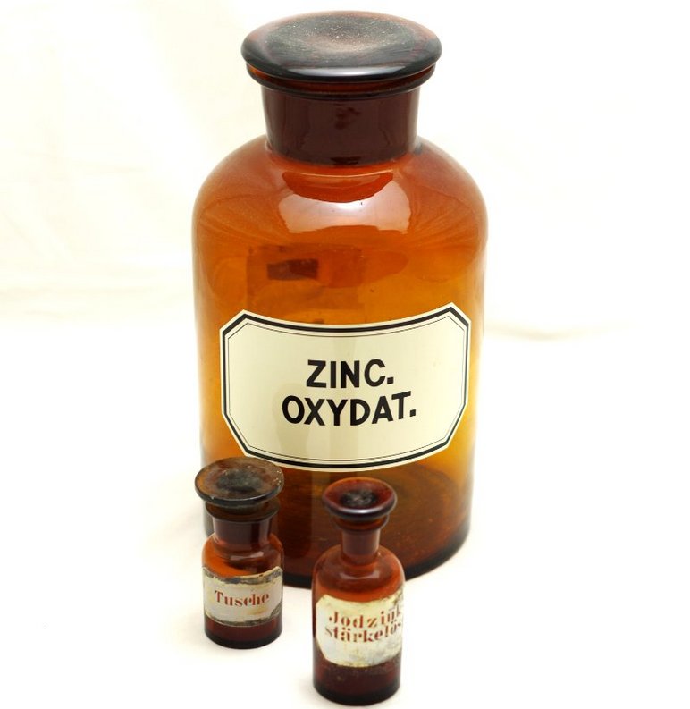 Drei historische Apotheker-Fläschchen aus braunem Glas, die größte ist etikettiert mit den Worten "Zinc Oxydat".