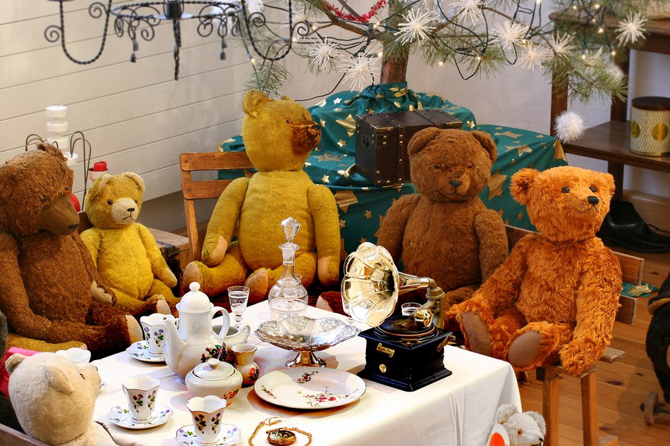 Das Foto zeigt sechs Teddybären, die an einer gedeckten Miniatur-Kaffeetafel sitzen. Neben dem Kaffeeservice steht auch ein Mini-Grammophon auf dem Tisch. Im Hintergrund ist ein Weihnachtsbaum zu sehen.