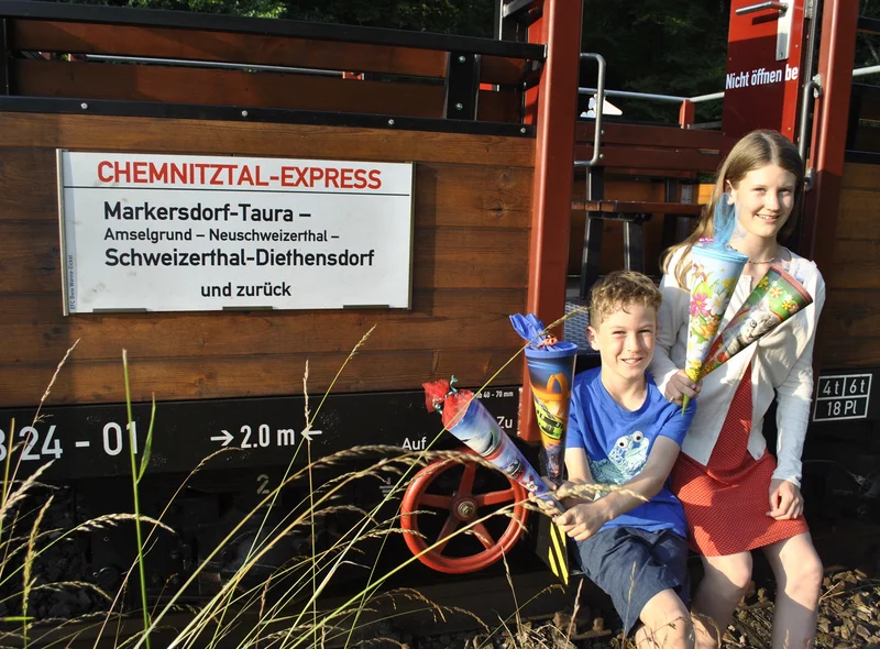 Ein Junge und ein Mädchen sitzen mit Zuckertüten auf dem offenen Wagen des historischen Chemnitztal-Express.