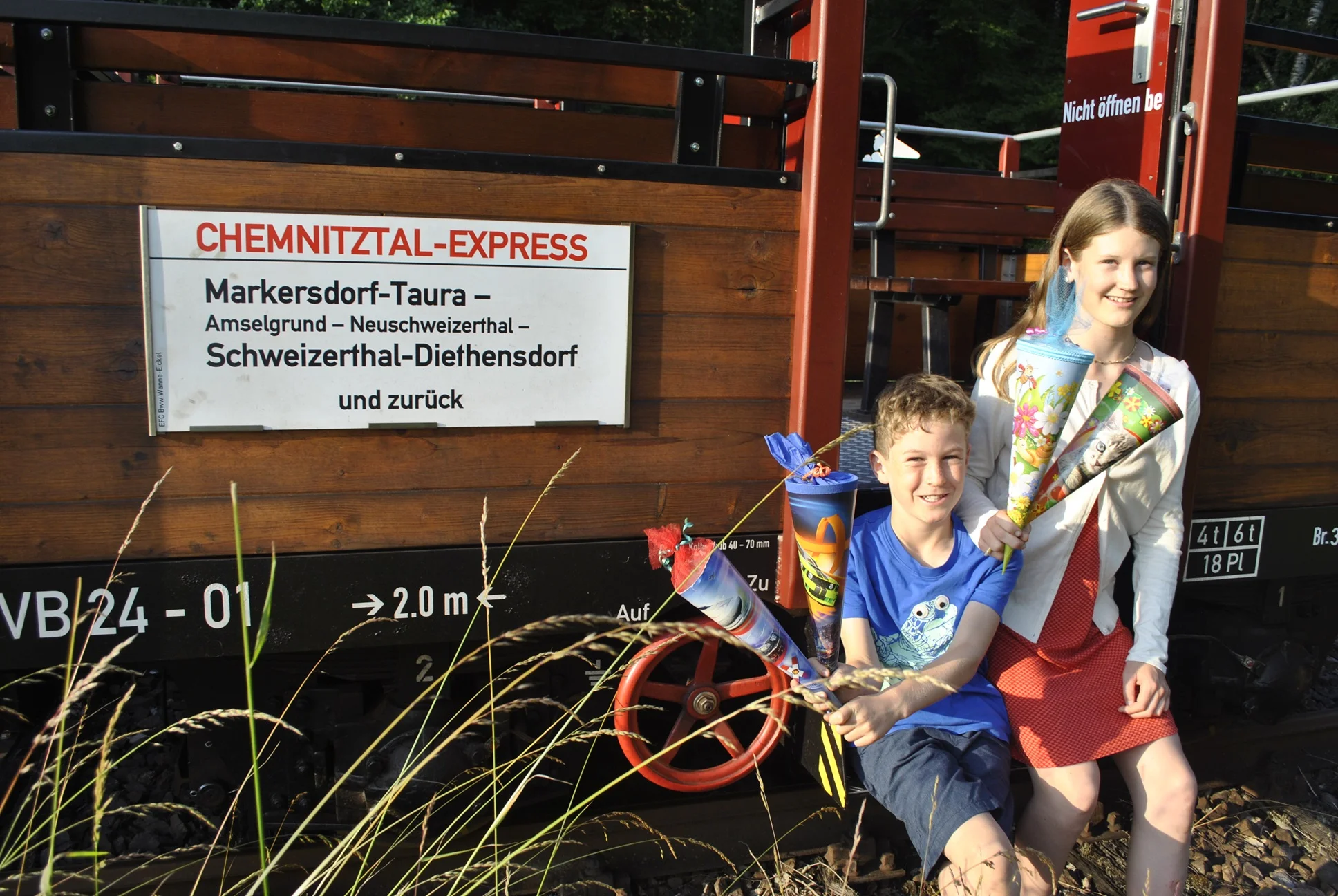 Ein Junge und ein Mädchen sitzen mit Zuckertüten auf dem offenen Wagen des historischen Chemnitztal-Express.