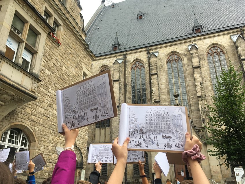 Das Foto zeigt die ausgestreckten Arme von Kindern, die vor der Thomaskirche in Leipzig Zeichnungen hochhalten.