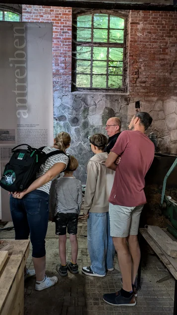 Eine Familie blickt auf das in der Mauer verbauten Wasserrad in der ehemaligen Mühlkammer