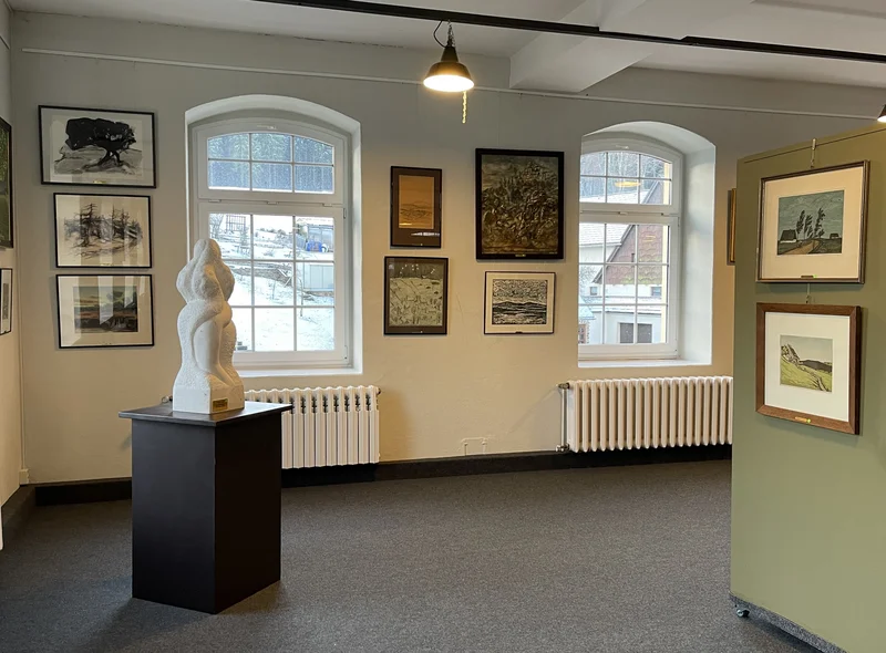Ausstellungsraum mit Landschaftsbildern zwischen großen Rundbogenfenstern; auf einem Sockel steht eine Skulptur.