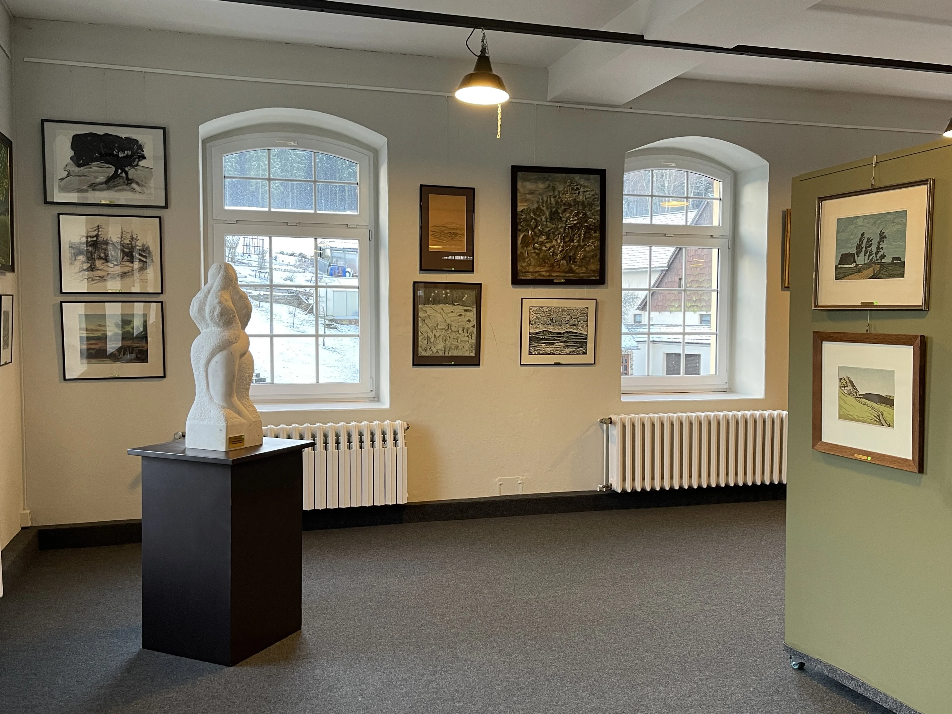 Kunstblicke auf das Erzgebirge Ausstellungsraum mit Landschaftsbildern zwischen großen Rundbogenfenstern; auf einem Sockel steht eine Skulptur.