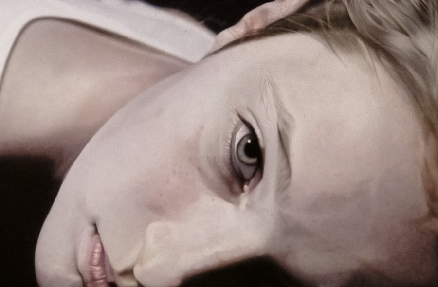 Fotorealistisches Gemälde des Gesichts einer auf dem Bauch liegenden jungen Frau, die den Betrachter von schräg unten anblickt