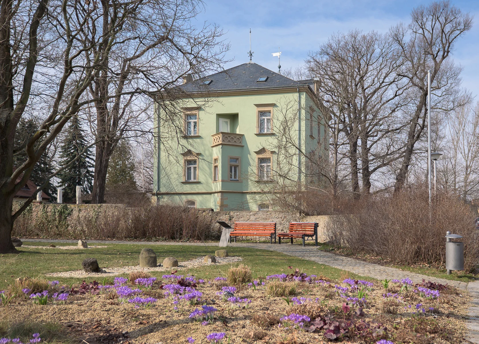 Die Karrasburg in Coswig Frühlingshafte Außenansicht eines in einem Park befindlichen, hellgrün getünchten, villenartigen Gebäudes; im Vordergrund violett blühende Krokusse