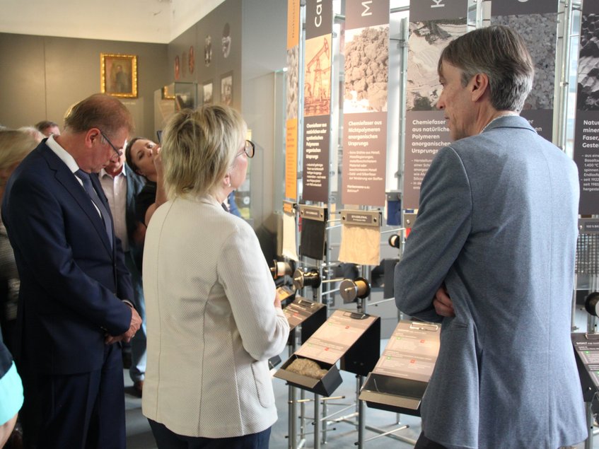 Von hinten sind eine Frau und zwei zu ihrer Linken und zu ihrer Rechten stehende Männer zu sehen, die ein Ausstellungsmodul betrachten.