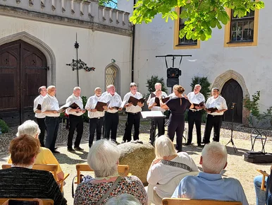 Muttertagskonzert im Schlosshof Hinterglauchau Ein kleiner Männerchor singt bei schönem Wetter im Freien. Das Publikum sitzt auf Stühlen unter einem Baum.