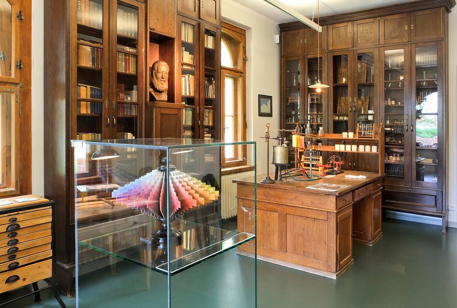 Blick in einen mit Holzschränken und einem großen Schreibtisch ausgestatteten historischen Raum, im Vordergrund der Ostwaldsche Doppelkegel in einer Vitrine