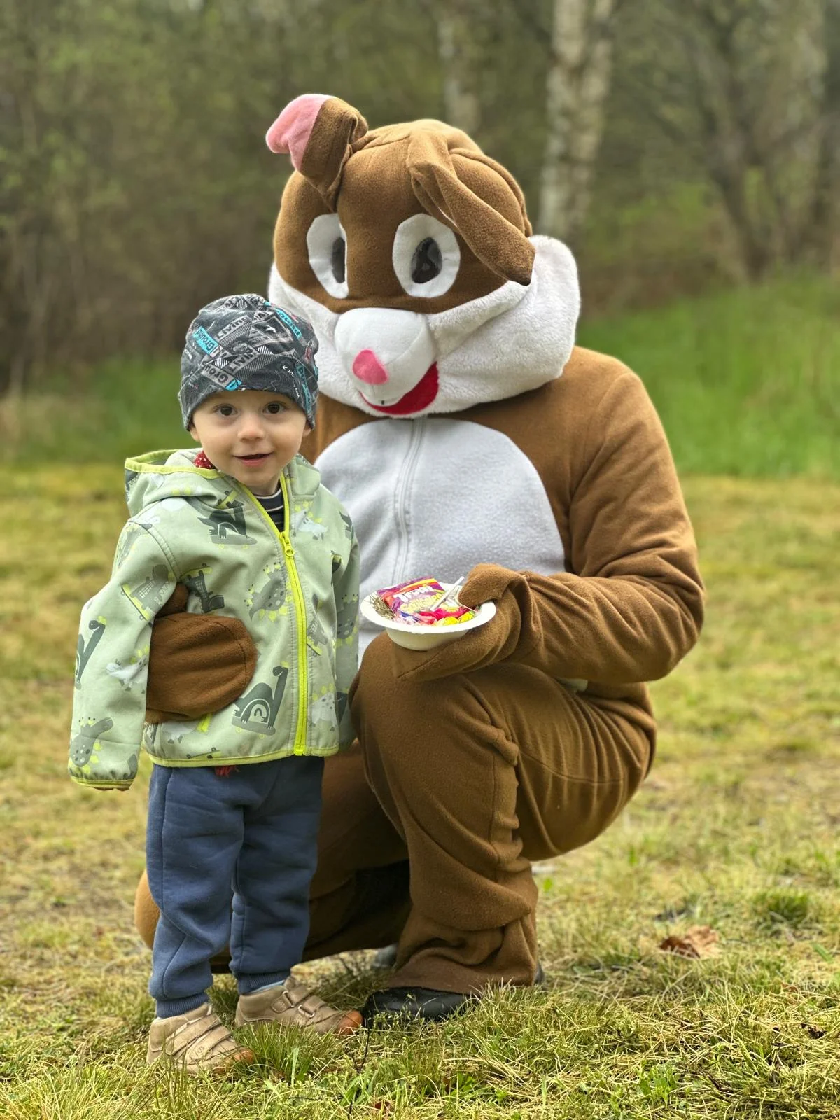 Ein als Osterhase verkleideter Erwachsener überreicht einem Kind ein Tellerchen mit Süßigkeiten.