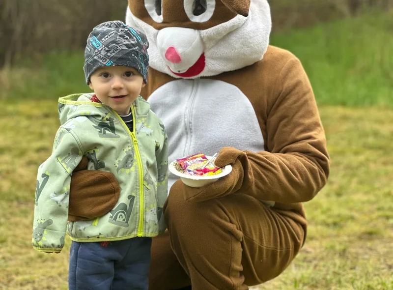 Ein als Osterhase verkleideter Erwachsener überreicht einem Kind ein Tellerchen mit Süßigkeiten.