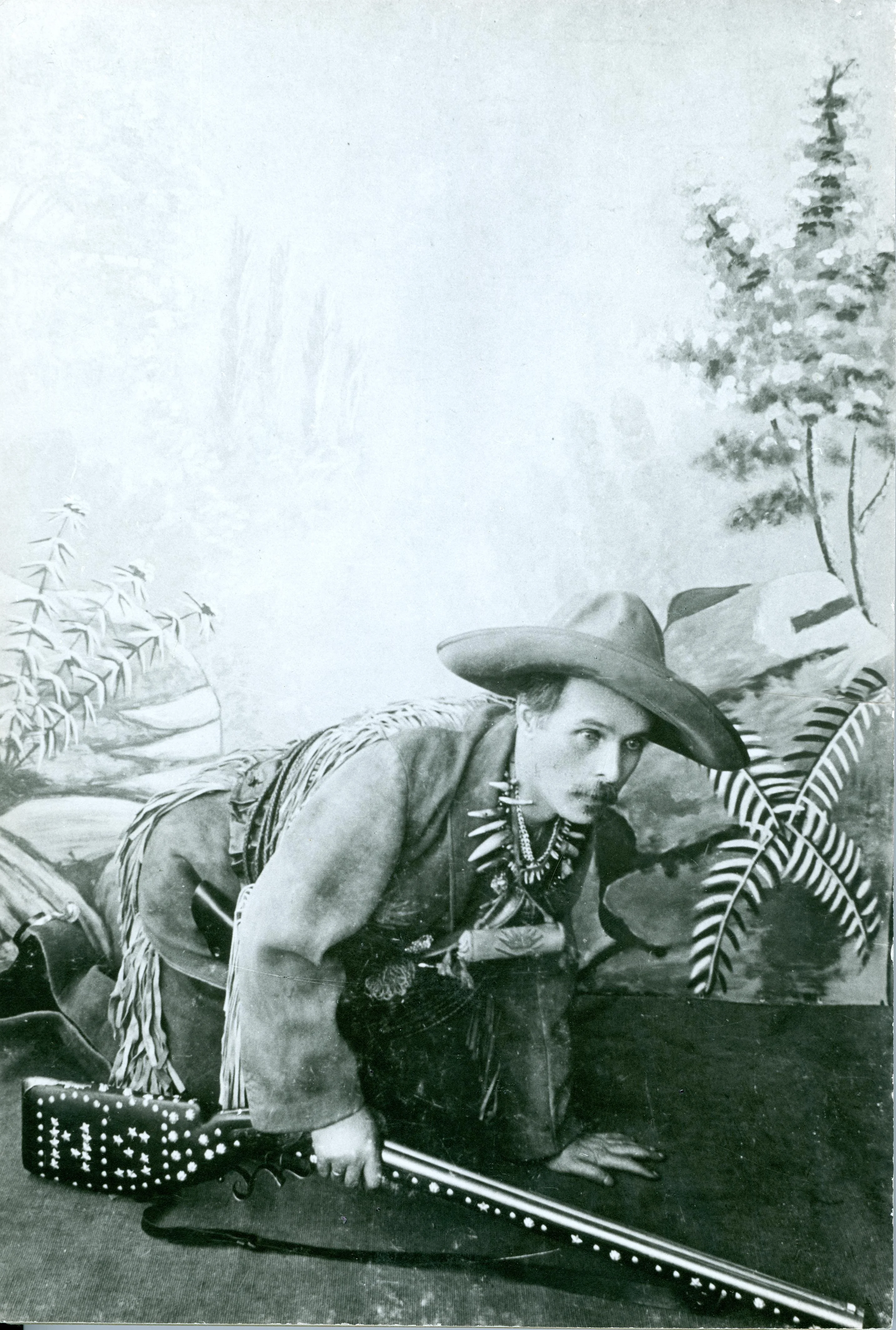 Ein als Cowboy verkleideter Mann auf allen Vieren, sich scheinbar anschleichend, in der rechten Hand ein Gewehr haltend