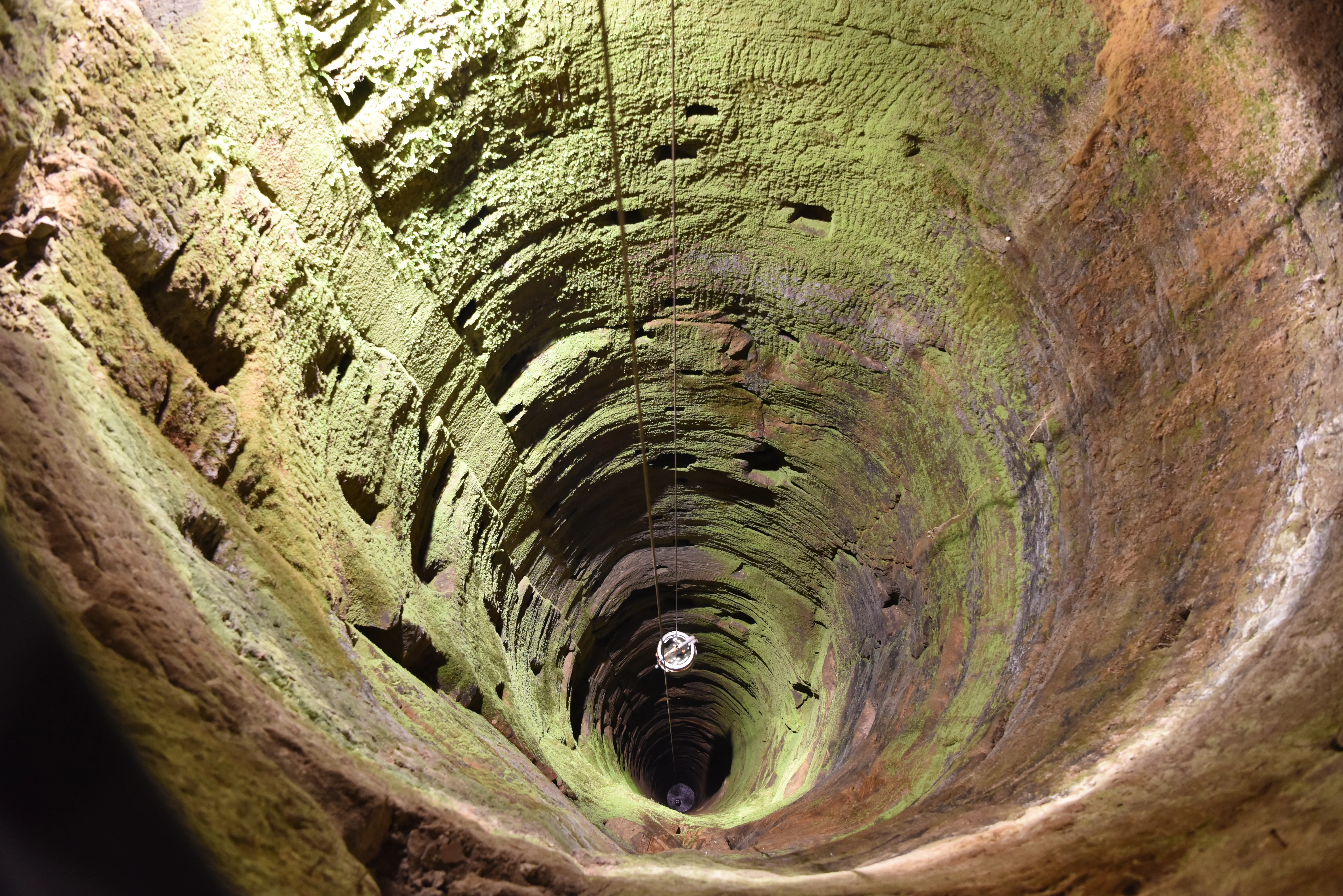 Beleuchteter Brunnenschacht der Festung Königstein. Ein gefülltes Wasserfass hängt an einem Seil und wird nach oben gezogen.
