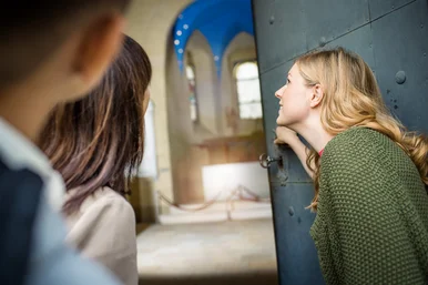 Sonderführung zum Tag des offenen Denkmals 2025 Drei Personen blicken durch eine halb geöffnete, alte eiserne Schlosstür in einen mit Rundbögen versehenen historischen Raum.