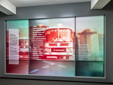 Das Foto zeigt eine große Ausstellungstafel mit einem verfremdeten, verschwommenen Bild eines Reisebusses und einem Text mit der Überschrift "Freikauf aus der DDR" und einem Zitat. Es lautet Zitat "Aber andererseits sind wir natürlich keine Dummköpfe und lassen unsere Gefängnisse voll mit irgendwelchen Schmarotzern, die wir sowieso nicht brauchen... Also alles muss politisch entschieden werden, durchdacht werden. Redebeitrag von Erich Mielke auf einer MfS-Dienstbesprechung vom 12. Februar 1987." Zitat Ende.