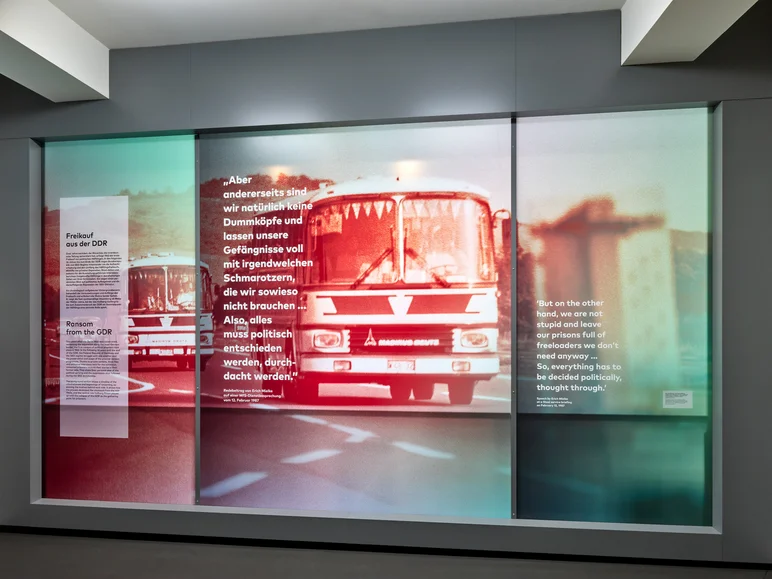 Das Foto zeigt eine große Ausstellungstafel mit einem verfremdeten, verschwommenen Bild eines Reisebusses und einem Text mit der Überschrift "Freikauf aus der DDR" und einem Zitat. Es lautet Zitat "Aber andererseits sind wir natürlich keine Dummköpfe und lassen unsere Gefängnisse voll mit irgendwelchen Schmarotzern, die wir sowieso nicht brauchen... Also alles muss politisch entschieden werden, durchdacht werden. Redebeitrag von Erich Mielke auf einer MfS-Dienstbesprechung vom 12. Februar 1987." Zitat Ende.