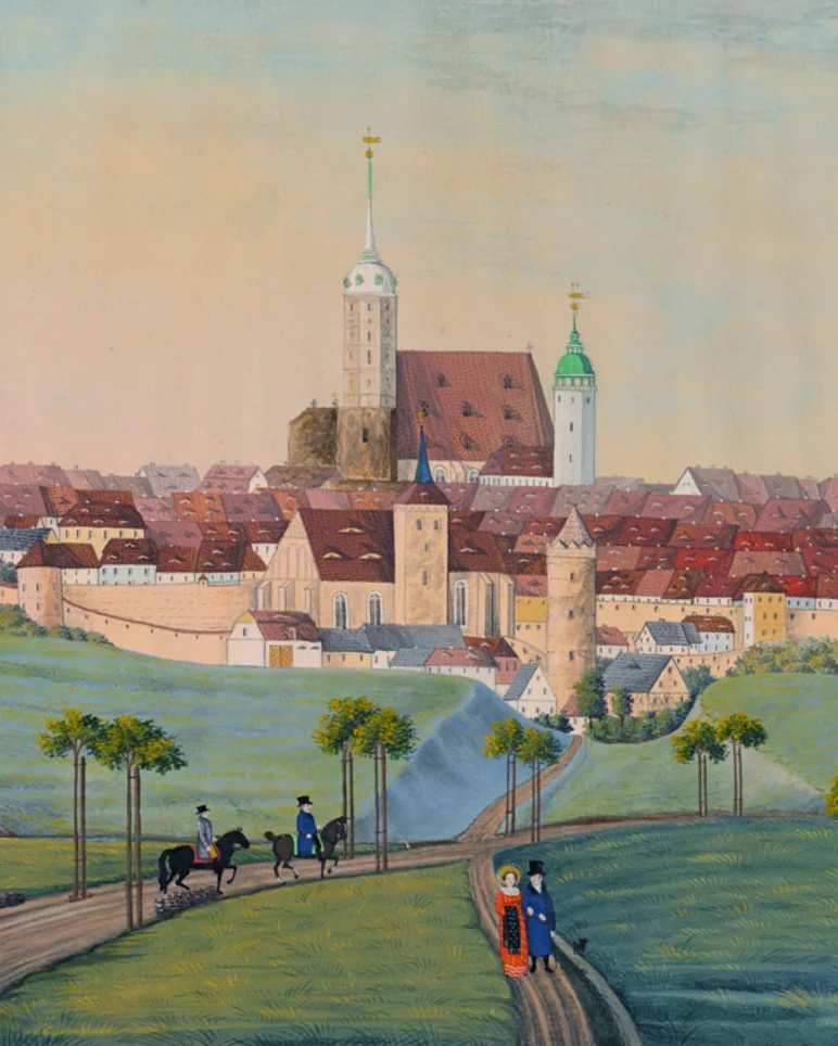 Türme, Dächer und die Mauer der Stadt Bautzen, davor grüne Wiesen und Wege, auf denen paarweise Personen zu sehen sind, die spazieren gehen oder reiten