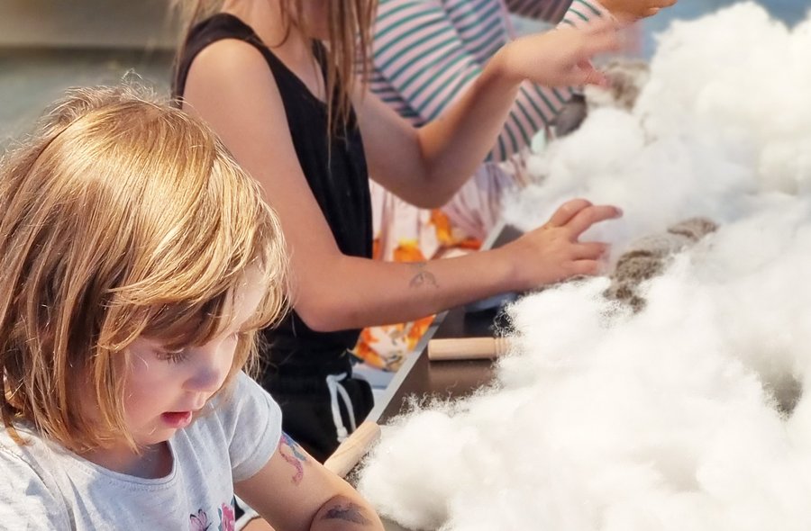 Drei Kinder haben fluffiges Ausstopfmaterial vor sich, das sie für ihre Kuscheltiere verwenden.