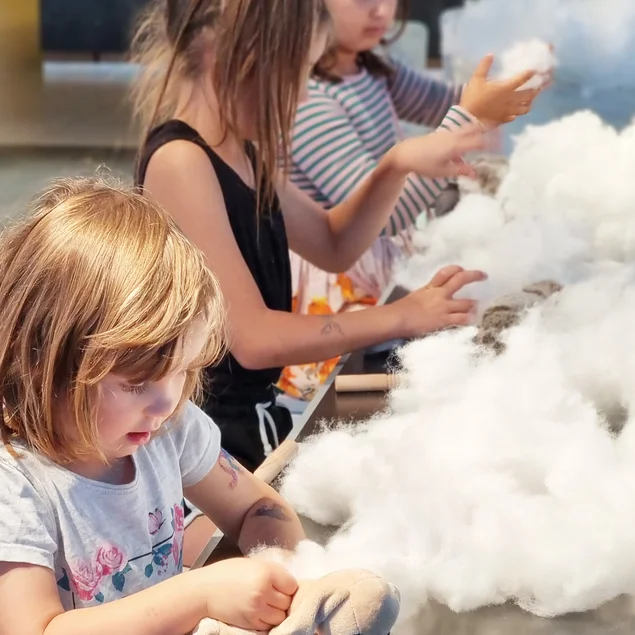 Drei Kinder haben fluffiges Ausstopfmaterial vor sich, das sie für ihre Kuscheltiere verwenden.