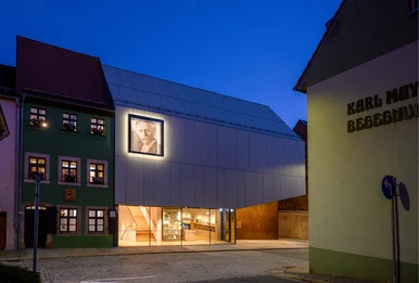 Das Foto zeigt eine Außenansicht des Karl-May-Hauses und des Museumsdepots bei Nacht. Der Eingangsbereichs des Museumsneubaus aus hell erleuchtet.